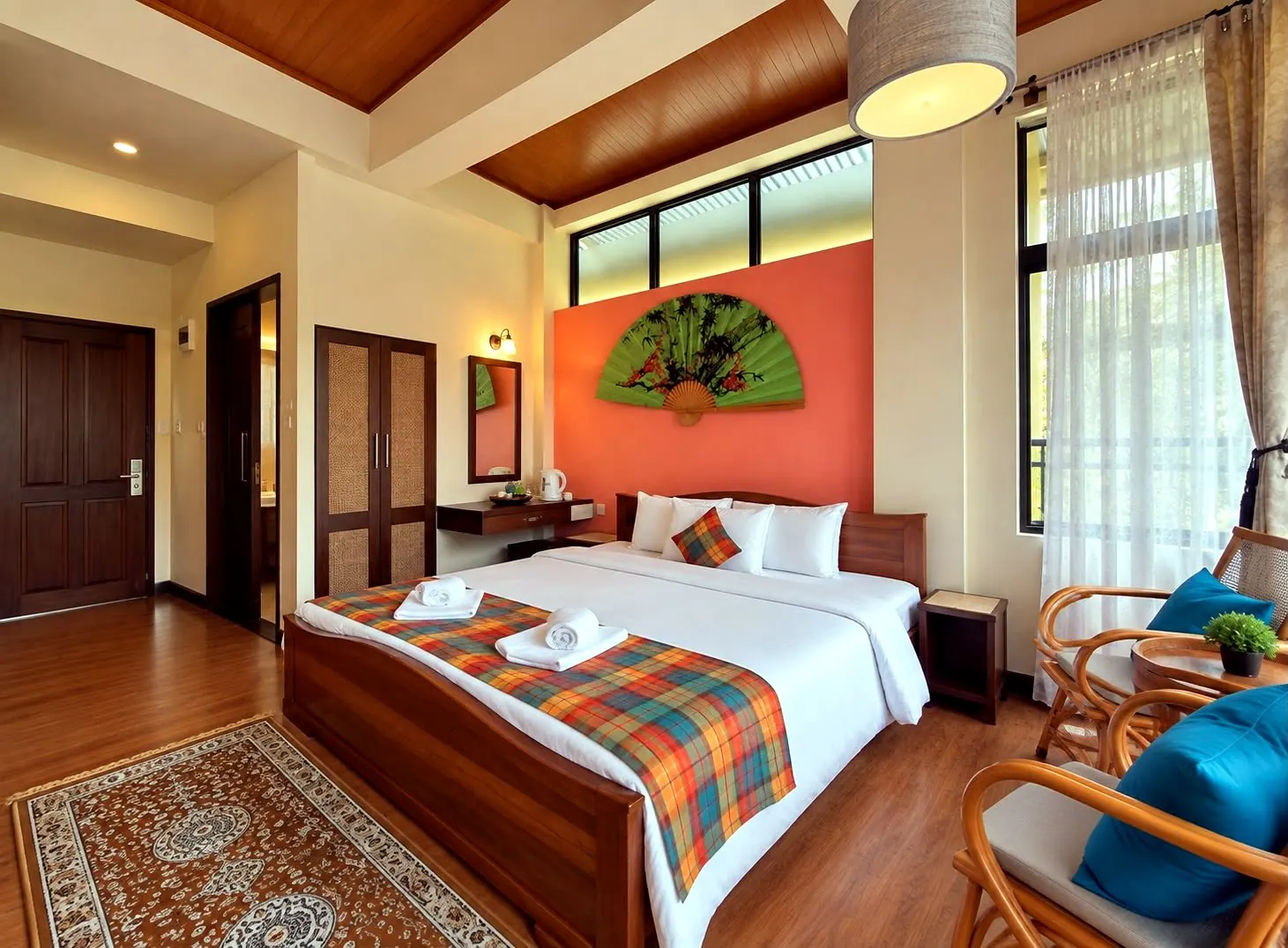 Pine room with a coral accent wall, a large green painted fan, and a private balcony beyond sheer curtains