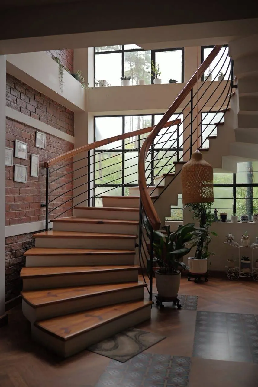 The staircase at Sha Ri Loum, seen from the ground floor, rising toward a wall of pine-facing windows